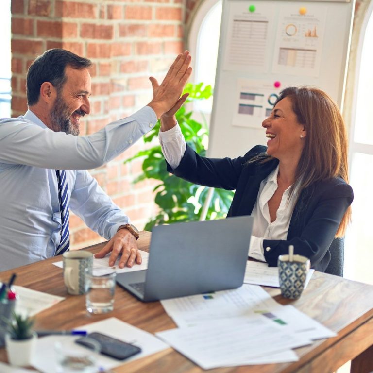 Businessman and businesswoman high-fiving in an office after a successful meeting